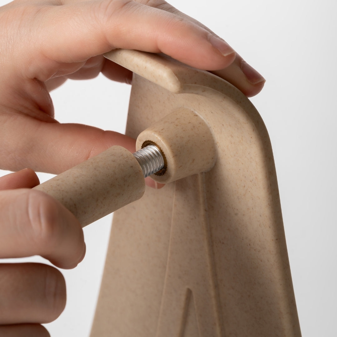 Hand holding a beige attachment for the Reliefboard, screwing it into place, against a white background